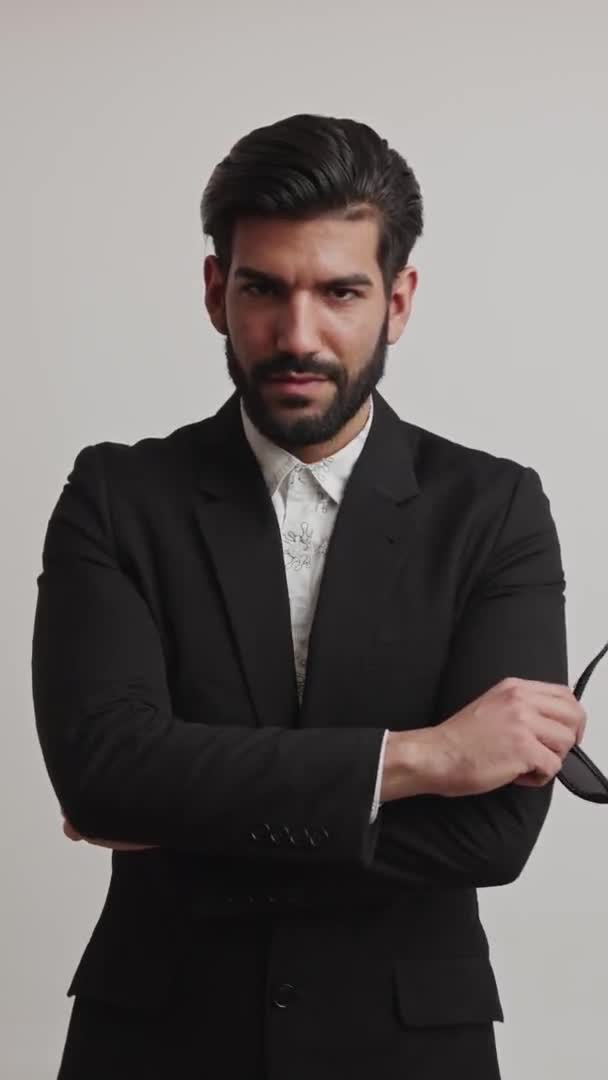 Vertikale mittlere Studioaufnahme eines sexy verführerischen bärtigen kubanischen Geschäftsmannes mit glänzenden Haaren, der in die Kamera blickt und seine Arme auf seiner Brust verschränkt. Grauer Hintergrund. — Stockvideo