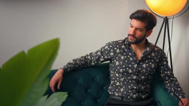 Sexy kubanischer Brunet sitzt auf einem grünen Sofa in seiner modernen Wohnung, denkt über seine Probleme nach und sieht leicht frustriert aus. — Stockvideo