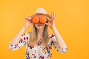 Sarışın genç bir kadın gözlerine portakal sürüyor. Sağlıklı yaşam tarzı, turuncu arka plan. Yakın çekim stüdyo fotoğrafı. 