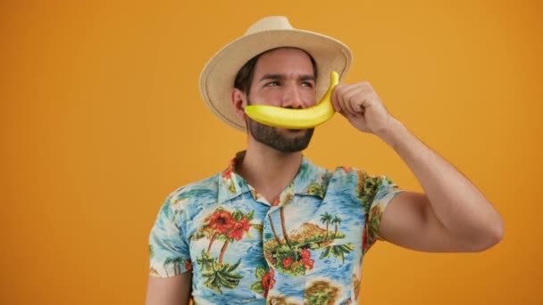 Schöner lateinischer bärtiger Mann in Bademode, der durch die Banane spricht und über den gelben Hintergrund lacht, Studio isoliert, mittlere Einstellung. — Stockvideo