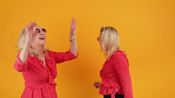 Deux femmes blondes caucasiennes avec des lunettes de soleil dansant et profitant de plan moyen studio plan orange concept de bien-être — Video