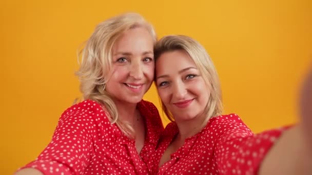 Laisse prendre un selfie - deux femmes heureuses européennes blondes prenant un selfie moyen gros plan studio tourné fond orange — Video