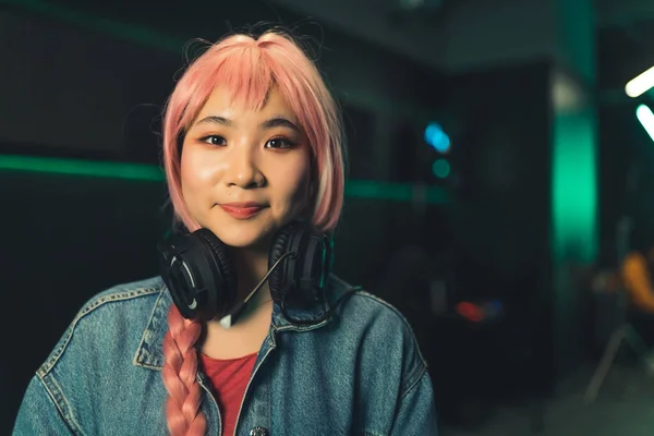 Portrait of young Asian woman with short pink hair wearing headphones dark background copy space — ストック写真