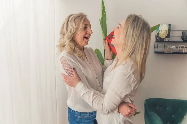Happy blonde mom hugging with her daughter while receiving a birthday gift —  Fotos de Stock