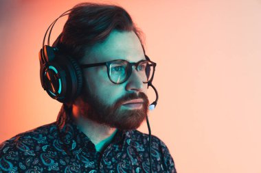 Büyük siyah kulaklıklara mikrofon takarak gömlek ve gözlük takan koyu renk saçlı bin yıllık bir adam. Stüdyo çekimi.