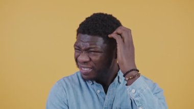 Confused thoughtful puzzled black guy in his 30s scratching his chin and head trying to remember something. Slose up studio shot on orange background.
