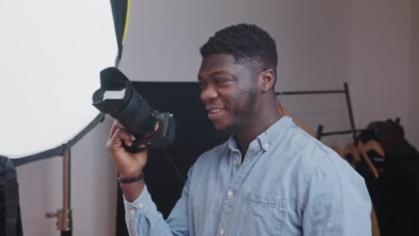 Excited middle-aged elegant african american man wearing a light blue shirt holding a professional camera pretending to take a picture. — Stok video