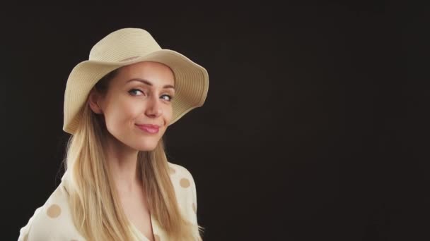 Stúdió lövés a fekete háttér egy aranyos fókuszált fiatal szőke európai nő bézs kalap és egy pontozott elegáns blúz. — Stock videók