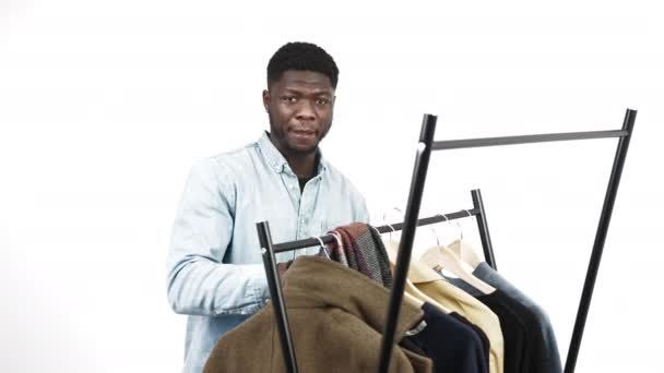 Orgulloso hombre negro elegante con una camisa de mezclilla recogiendo un traje de un estante de ropa de pie. Primer plano plano del estudio. — Vídeo de stock