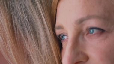 Close-up shot of a middle-aged caucasian wrinkled woman, looking away, closing her eyes, wearing makeup, blue eyeshadow, pink lipstick, leaning her head towards an unrecognizable person.