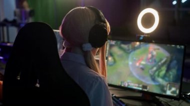 Back shot of a young concentrated teenage girl looking at a computer screen, playing a esport cyber game with a lamp for live streams.