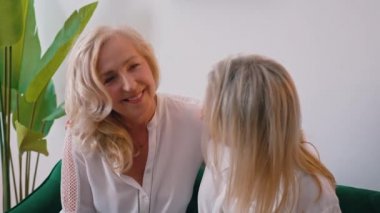 Avrupalı sarışın, aynı şekilde giyinmiş, koyu yeşil bir kanepede oturan, birbirine sarılan ve kahkahalarla gülen kadınlar..