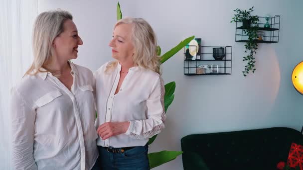 Vzrušené výrazné blondýny po čtyřicítce, které se na sebe dívají, jak stojí v moderním minimalisticky zařízeném obývacím pokoji, usmívají se a mluví. — Stock video
