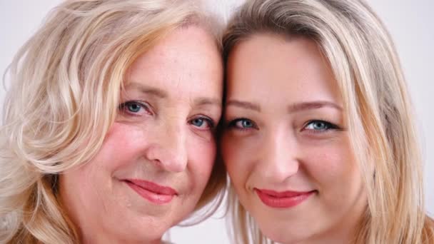 Gros plan studio tourné sur fond blanc de deux femmes caucasiennes blondes aux yeux bleus regardant une caméra toucher la tête et sourire. — Video