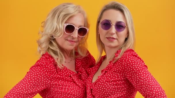 Dos hermosas mujeres europeas rubias de unos 40 años de edad, paradas una junto a la otra con camisas rojas y gafas de sol similares. Una mujer mostrando pulgares hacia arriba signo. — Vídeos de Stock