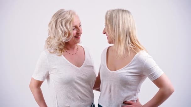 Mother and daughter like sisters wearing similar clothes standing close to each other and laughing. Studio shot on white background. — Vídeos de Stock