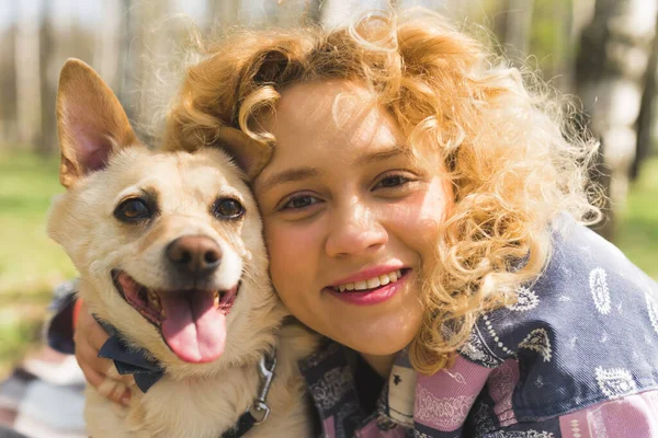 Outdoor close-up portrait of a joyful beautiful natural caucasian woman with curly blonde hair and a mixed-breed happy dog. — Zdjęcie stockowe
