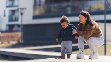 İlkbahar. Genç, esmer anne, çok ırklı oğlunu kaldırımda tutuyor. Aile güneşli havanın tadını çıkarıyor.