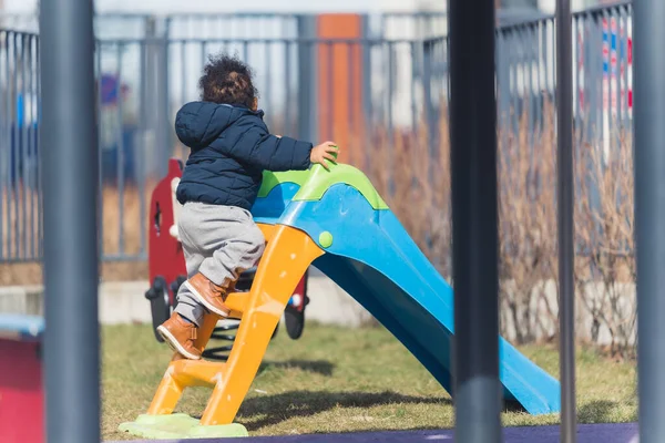 Little biracial boy climbing on the playground slide. Child curiosity concept. Springtime vibes. — 图库照片