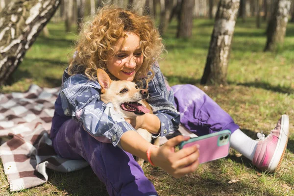 Beautiful young girl in casual clothes is making a selfie with her cute dog while sitting outdoors, both smiling — Zdjęcie stockowe
