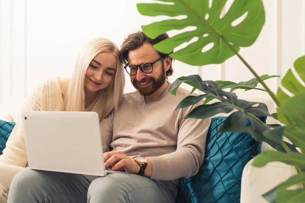 Mid aged european joyful couple sitting on a couch holding a laptop doing online shopping. — Stockfoto
