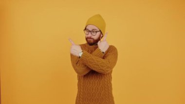 young Caucasian man hesitating pointing sideways with arms crossed orange background medium shot copy space studio shot 