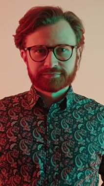 Genç beyaz adam gözlüğü düzeltiyor. Orta boy, dikey video stüdyosu. Pembe arka plan.