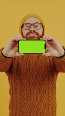 Telefona bak. Cep telefonunu boş gösteren genç adam. Portakal rengi arka plan stüdyosu.