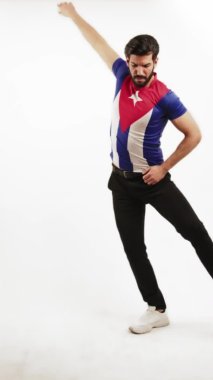 Latin asıllı yakışıklı bir adamın Küba bayraklı tişört giyip Latin dansı hareketleri gösteren dikey bir stüdyo resmi..