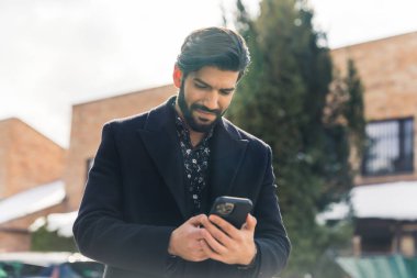 Genç Latin bir adam dışarıda telefonuyla mesaj atıyor.