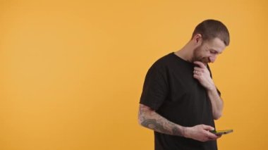 Dövmeli yakışıklı adam kameraya bakıp gülümsüyor ve sarı arka plan izole edilmiş stüdyo çekimlerinde fotokopi çekiyor. 