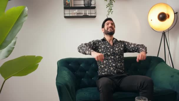 Розслаблений латинський красивий хлопець відчуває себе щасливим і вільним, сидячи на дивані в елегантній квартирі з широко відкритими руками . — стокове відео