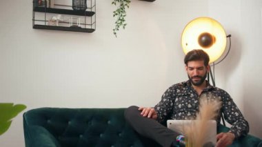 30 'lu yaşlarında Kübalı stil sahibi bir adam oturma odasında bir lambanın yanında oturuyor, online bir toplantı yapıyor, konuşuyor ve gülüyor..