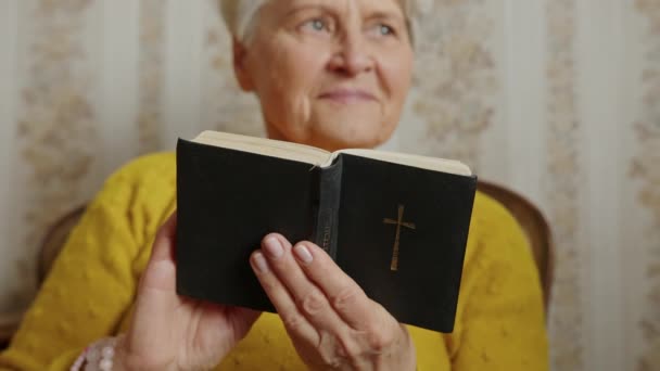 Dankbare senior vrouw het lezen van de bijbel in de woonkamer medium close-up religie concept — Stockvideo