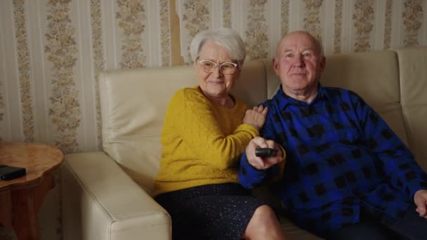 Glad äldre kaukasiska par tittar på TV hemma äldre människor koncept medium full shot inomhus — Stockvideo