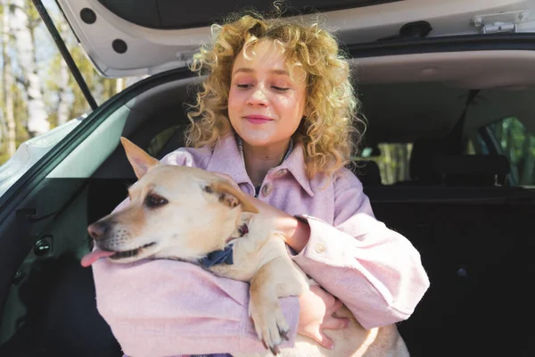 Wesoły piękny dziewczyna pieszczoty jej pies w samochodzie — Zdjęcie stockowe