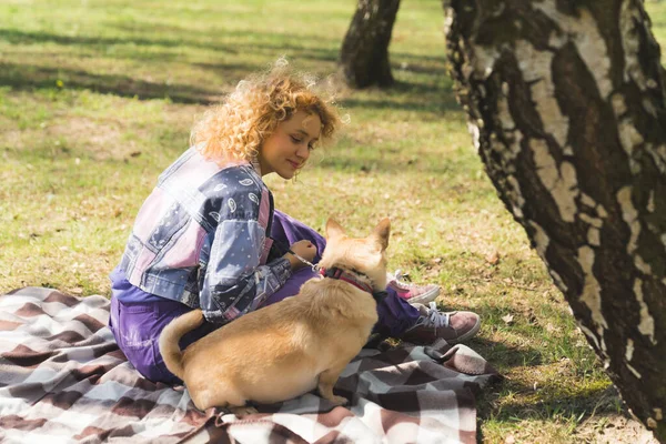 Härligt foto av en vacker flicka med sin hund sitter på blancket i parken — Stockfoto