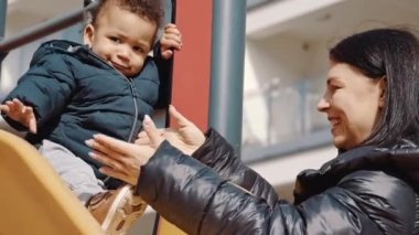 Afro-Amerikalı çocuk ve anne oyun parkındaki tavşan tepesinde oynuyorlar. 