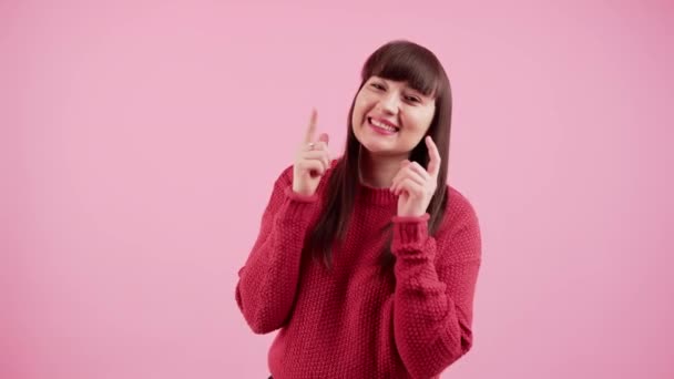Glada kaukasiska tusenåriga flicka röra hennes kinder i en söt kawaii sätt när du står i en studio över rosa bakgrund i en mysig röd tröja. — Stockvideo