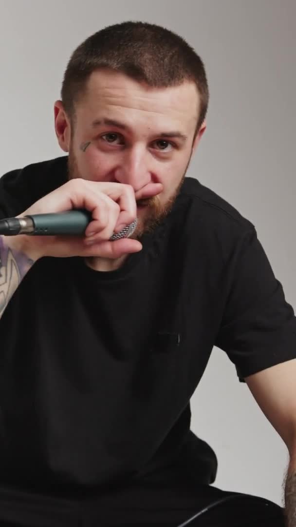 Вертикальний студійний знімок татуйованого музиканта середнього віку, який дзвонить на свій мікрофон і дивиться на камеру. Віддаючи мікрофон аудиторії, щоб співати з ним . — стокове відео