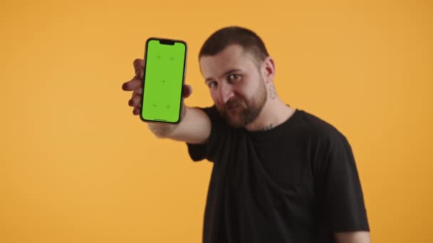 Streetwise kaukasiska manligt tatuerad kille som visar grön skärm mock-up smartphone och skärpa musklerna över gul bakgrund. — Stockvideo