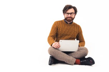 Dost canlısı, yakışıklı, tıraşsız, bin yıllık beyaz bir adam stüdyoda dizinde dizüstü bilgisayarla oturuyor. Beyaz arkaplan stüdyosu kopya alanı.