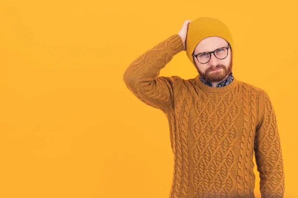 Confusión. Guapo barbudo hipster en un gorro y suéter de punto tocando su cabeza y pensando en sus problemas actuales sobre fondo amarillo. —  Fotos de Stock