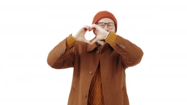 Hipster hombre caucásico en ropa interior de otoño marrón haciendo símbolo del corazón con ambas manos sobre fondo blanco. Grabado en estudio. espacio de copia. — Vídeo de stock