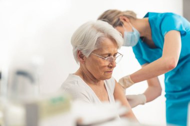 Sarışın kadın doktor, göz korkutulan yaşlı bir hastaya koronavirüs aşısı yapıyor. İç çekim