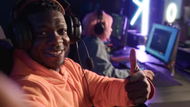 Ενθουσιασμένος χαρούμενος Αφροαμερικάνος με μεγάλα ακουστικά και μικρόφωνο που βγάζει selfie κατά τη διάρκεια ενός τουρνουά βιντεοπαιχνιδιών, δείχνοντας μια πινακίδα εντάξει. — Αρχείο Βίντεο