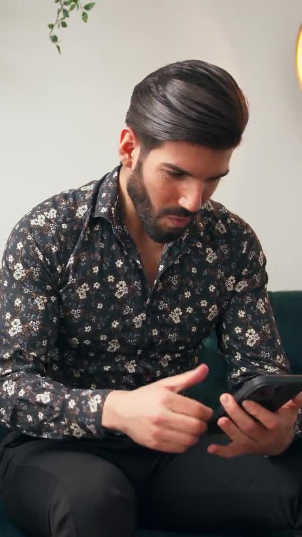 Gut aussehender kubanischer bärtiger Mann in seinen Zwanzigern, der auf einem Sofa in einem Wohnzimmer sitzt und sein Telefon hält, um eine Online-Lotterie zu gewinnen. — Stockvideo