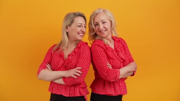 Dos mujeres alegres atractivas en sus 40 años en trajes similares, paradas espalda con los brazos cruzados, sonriendo y riendo. — Vídeo de stock