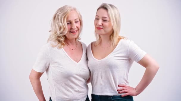 Studio skjuten på vit bakgrund av två liknande ser medelålders kvinnor, står nära varandra placera sina händer på höfter. — Stockvideo