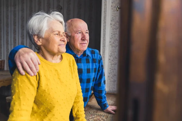 Söta äldre kaukasiska par tittar ut genom fönstret och ler medium shot inomhus senioritet koncept — Stockfoto
